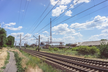 A blue sky with feathery clouds, a green grass along the railway and an old dilapidated plant in...