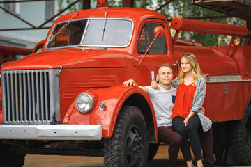 Vintage firefighting truck and a couple in love. Outdoor portrait of a beautiful young white girl and a handsome guy posing near old fire engine.