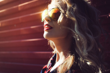 portrait of a girl close-up of a beautiful young sexy blonde in a red plaid shirt and shorts denim in sunglasses smiling and posing on the Sunset hipster - Powered by Adobe