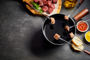 Five beef skewers held over fondue pot