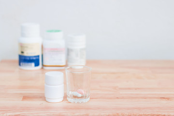 Bottles of medicine capsules and pills in small glass on wooden floor. With copy space.