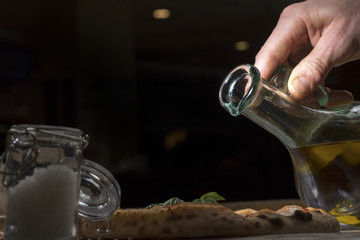 una mano versa da un oliera da tavola , dell'olio d'oliva su una pizza 