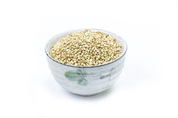 Dry buckwheat in white ceramic bowl isolated on white. Spilled buckwheat.