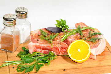 Two appetizing pieces, pork entrecote on a wooden cutting board with salt shaker and pepper and rosemary and lemon