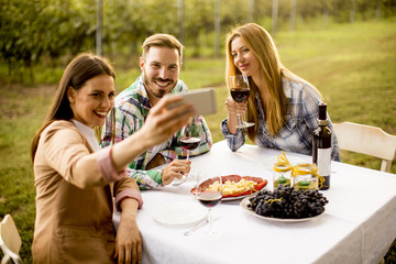 Young people sitting by the table and drinking red wine in the vineyard