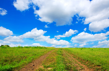 Fototapeta na wymiar Field road with green grass and blue sky with clouds.