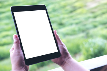 Fototapeta na wymiar Mockup image of woman's hands holding black tablet pc with blank white screen and green nature background