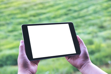 Mockup image of woman's hands holding black tablet pc with blank white screen and green nature background