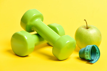 Obraz na płótnie Canvas Apple in greenish yellow color near dumbbells and measuring tape