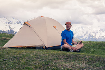 Tired man traveler sits next to the tent, in the mountains