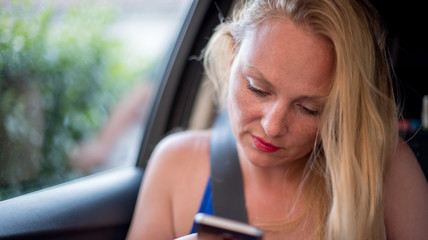 Fototapeta na wymiar Attractive blonde girl uses smartphone in the car