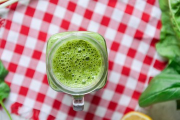 Top view Healthy green spinach smoothie in a jar mug with ingredients on the checkered napkin on the white marble table. Selective focus.