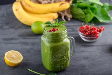 Healthy green spinach smoothie in a jar mug decorated with mint and red currant berries with ingredients on the black wooden table. Selective focus. Detox concept.