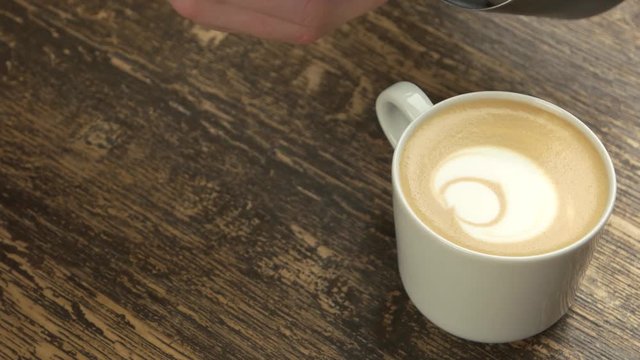 Barista making latte art bear. Frothy coffee in white mug.