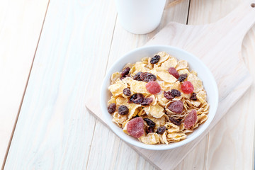 cornflakes and dry berry fruits in a white bowl on a wooden background.