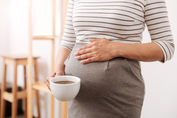 Plerasant pregnant woman holding a cup of coffee