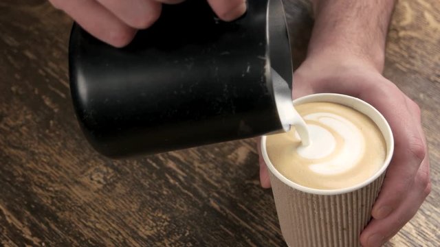 Hands of man, latte art. Coffee in paper cup, wood.