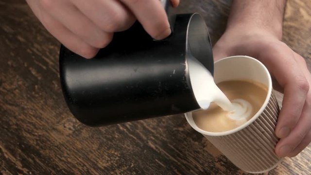 Hands making latte art flower. Coffee in paper cup.