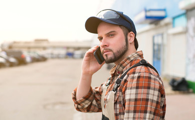 Young attractive white male in overalls and a plaid shirt and blue hat, talking on a cell phone...