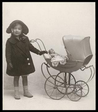 Little girl with toy pram and doll.. Date: circa 1905