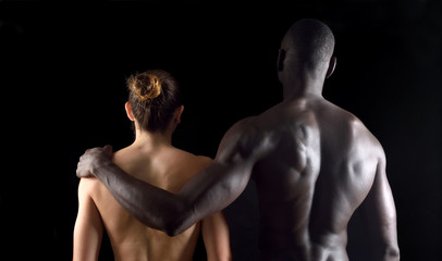 The embrace of an interracial couple on black background
