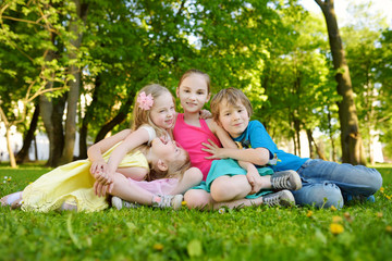 Naklejka na ściany i meble Four cute little children having fun together on the grass on a sunny summer day. Funny kids hanging together outdoors