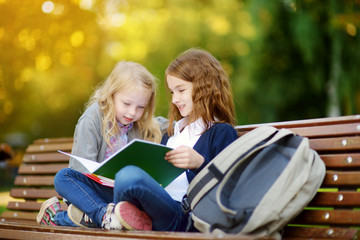 Fototapeta na wymiar Adorable little schoolgirls studying outdoors on bright autumn day. Young students doing their homework. Education for small kids.