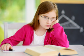 Stressed and tired schoolgirl studying with a pile of books on her desk