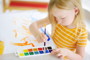Cute little girl drawing with colorful paints at a daycare. Creative kid painting at school.