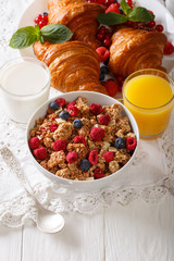 Healthy food: multigrain granola, croissants, fresh berries, milk and orange juice close-up. vertical