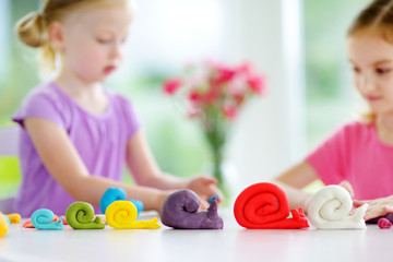 Two cute little sisters having fun together with colorful modeling clay at a daycare. Creative kids molding at home.