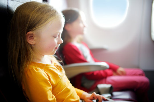 Two adorable little girls traveling by an airplane. Children sitting by aircraft window and looking outside.