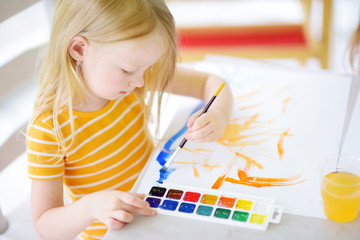Cute little girl drawing with colorful paints at a daycare. Creative kid painting at school.