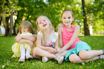 Naklejka na ściany i meble Three cute little sisters having fun together on the grass on a sunny summer day. Funny kids hanging together outdoors.