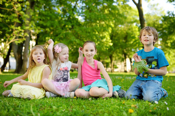 Fototapeta premium Four cute little children having fun together on the grass on a sunny summer day. Funny kids hanging together outdoors