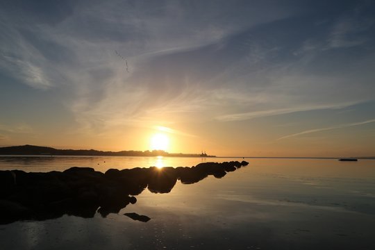 malerischer Sonnenaufgang mit blauem Himmel an einer Buhne an der Ostsee 