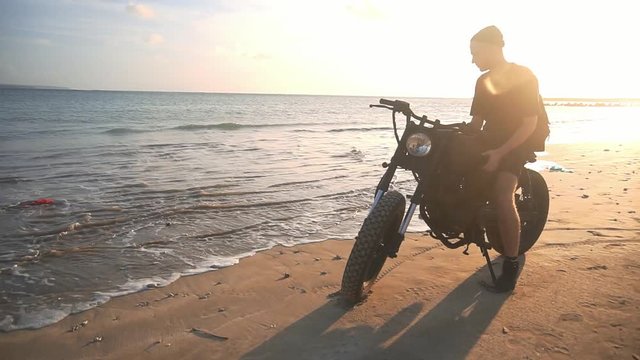 Motorcyclist starting to drive his motorbike on the beach during sunset, slow motion