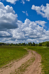 Fototapeta na wymiar Country road through the field. Sky with clouds