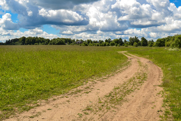 Country road through the field. Sky with clouds