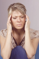 Young woman sitting on a couch, holding her head, having a strong headache