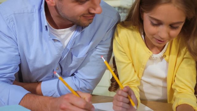 Close up portrait of cute young curly hair girl and her father drawing the picture at the kitchen.
