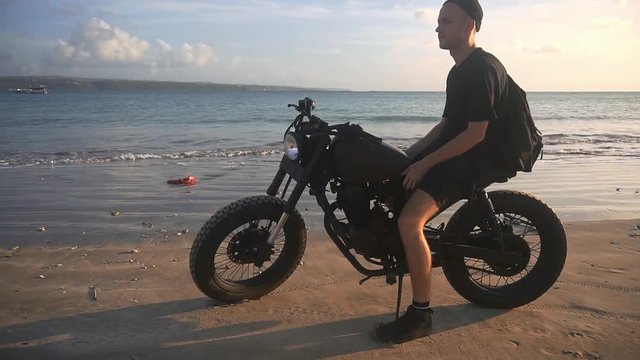 Motorcyclist starting to drive his motorbike on the beach during sunset, slow motion