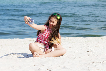 girl and dog make selfie on phone on the beach