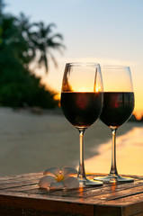 Romantic beach scene: two glasses of red wine at sunset near water