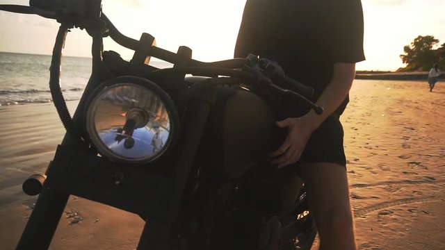 Motorcyclist starting to drive his motorbike on the beach during sunset, slow motion