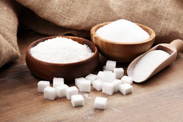 Bowl and scoop with white sand and lump sugar on brown wooden background