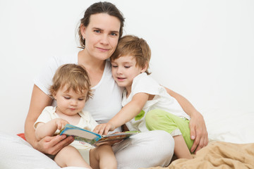 Obraz premium mother reads the book to two of her children the book in a bed. The happy family spends time together at home. 