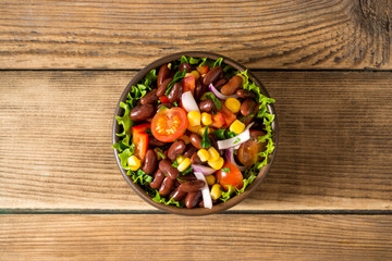 Fresh vegetable salad with beans in ceramic bowl on wooden table.