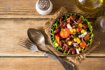 Fresh vegetable salad with beans in ceramic bowl on wooden table.