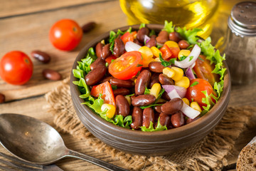 Fresh vegetable salad with beans in ceramic bowl on wooden table.